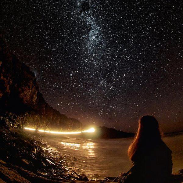 Jeune femme assise bord de mer nuit lumiere phares ciel etoile superbe